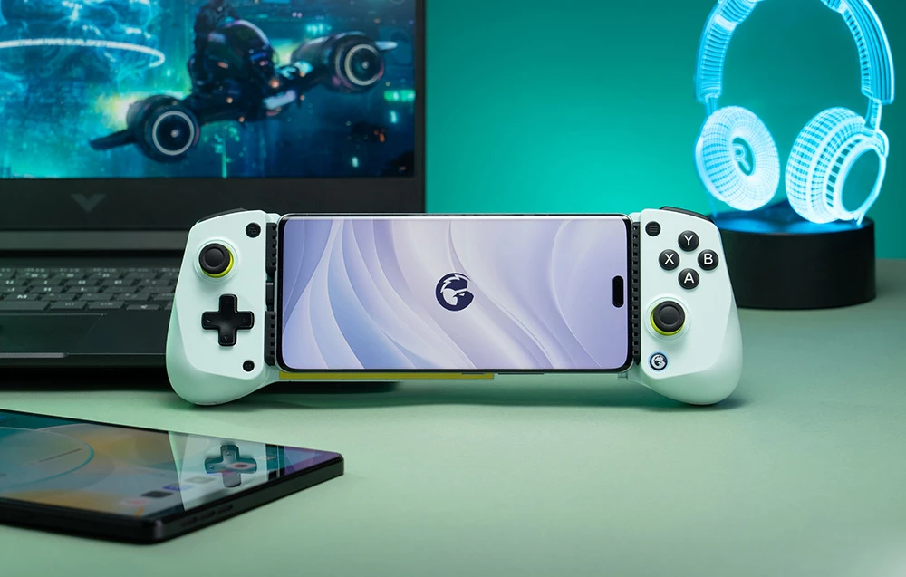 Smartphone montat într-un controller GameSir alb, amplasat în fața unui laptop și a unei lumini în formă de cască.
