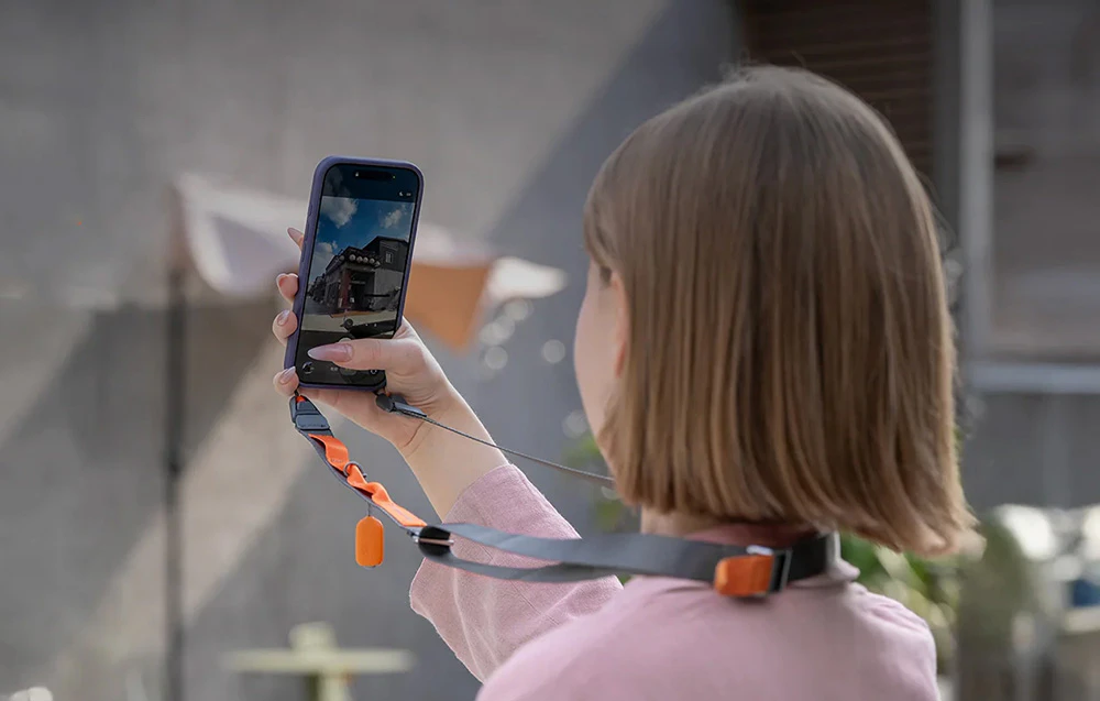 O femeie fotografiază o clădire cu smartphone-ul său montat pe o curea de gât PGYTECH