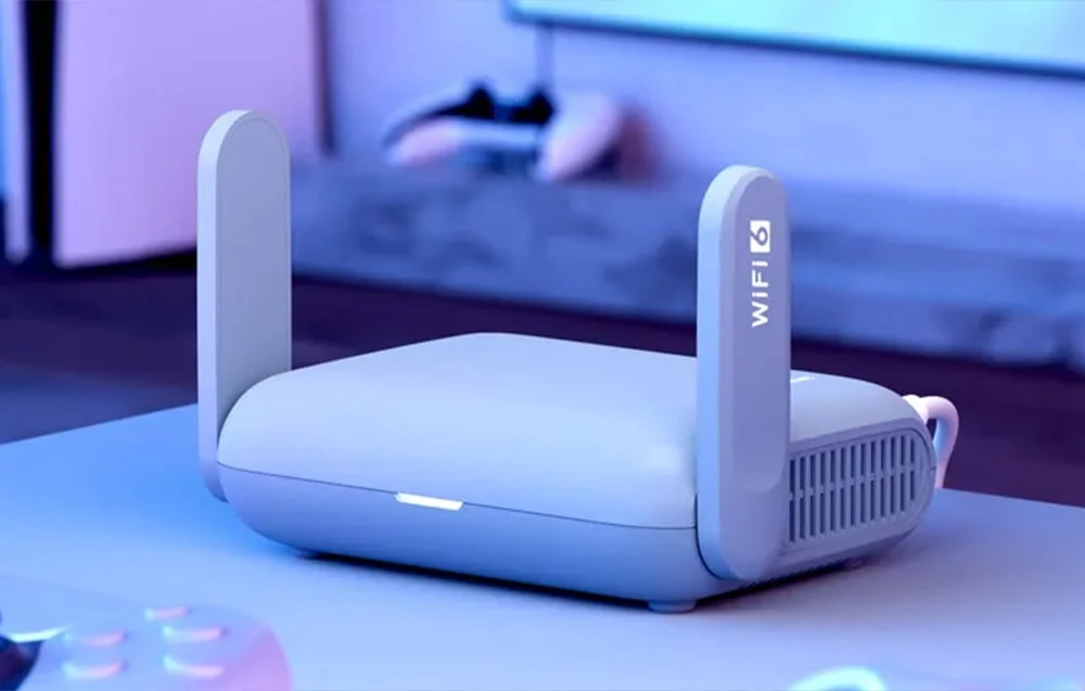 Un router de culoare deschisă se află pe un birou lângă o consolă de jocuri, într-o cameră iluminată de o lumină albastră