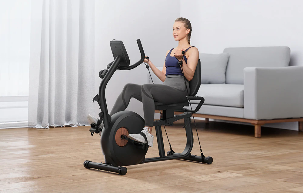 Femeie care face exerciții fizice pe o bicicletă Merach și folosește cabluri de rezistență