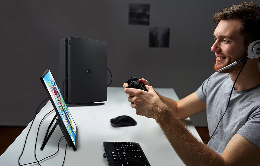 Un bărbat care se joacă pe o consolă PlayStation folosind un monitor portabil și o cască