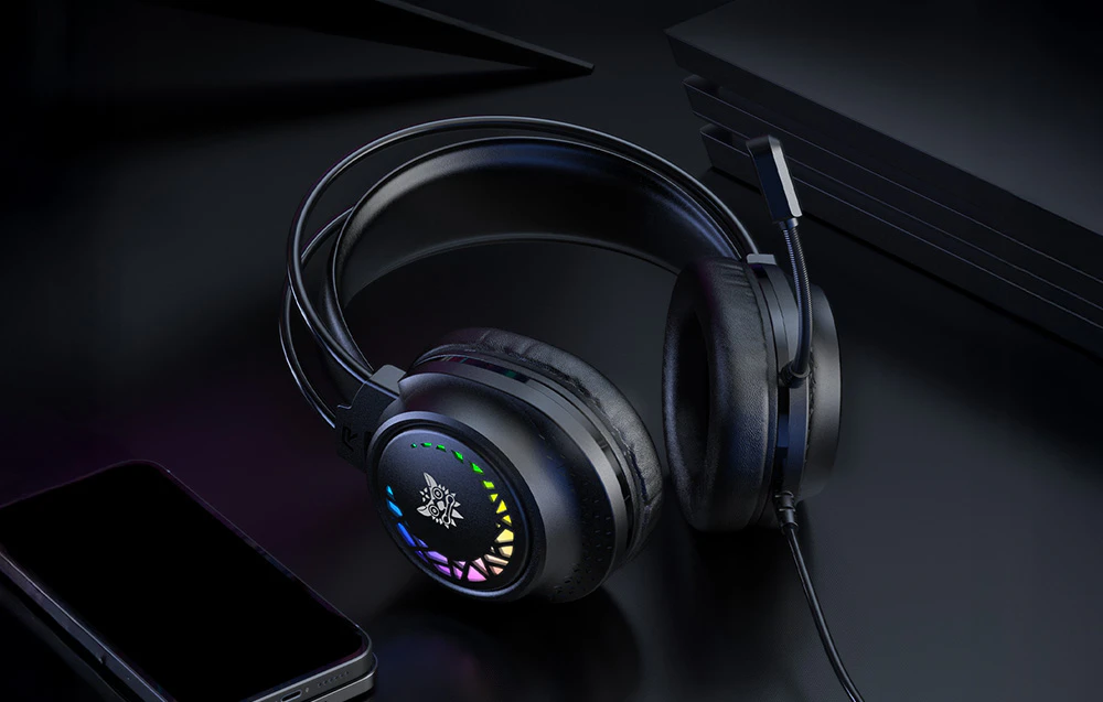 Căști negre over-ear cu retroiluminare colorată așezate pe un blat întunecat lângă un smartphone