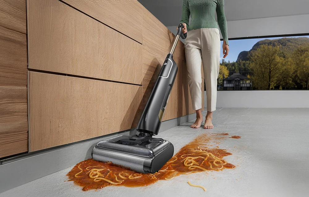 O femeie care folosește un aspirator pentru a curăța spaghetele vărsate cu sos de roșii într-o bucătărie modernă