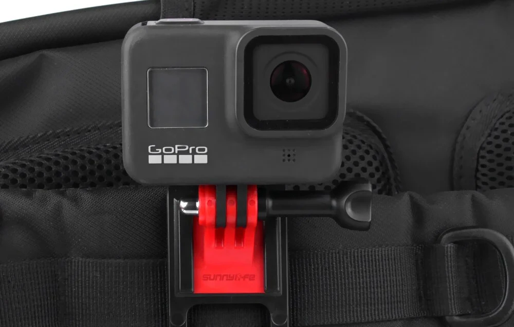 Cameră GoPro montată în clip roșu pe cureaua neagră a rucsacului, vedere din față a camerei