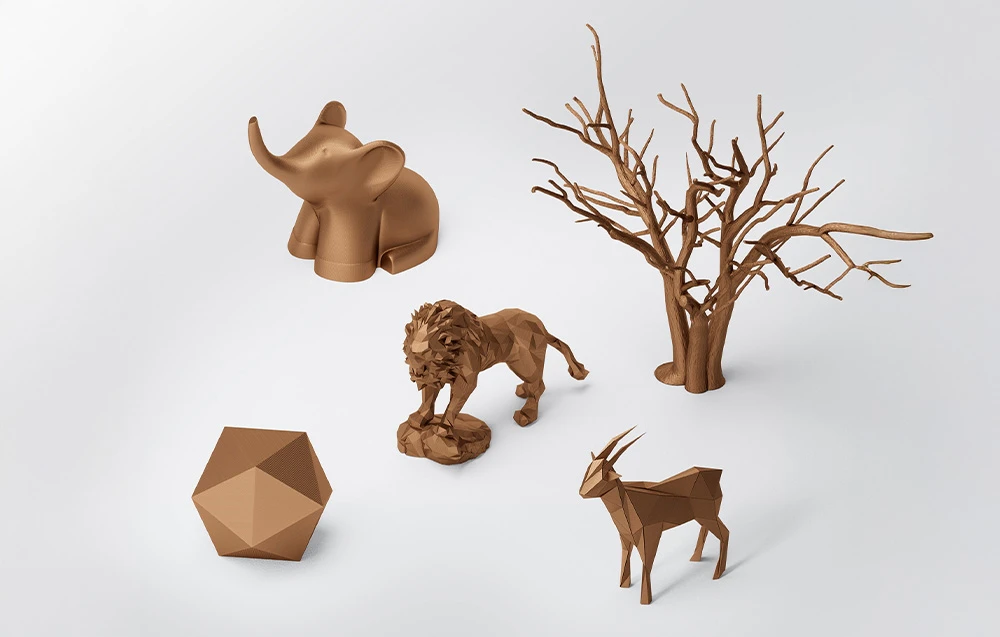 Colecție de figurine imprimate 3D în culoarea aramă, reprezentând un elefant, un leu pe o stâncă, un icosaedru geometric, un copac desfrunzit și o antilopă