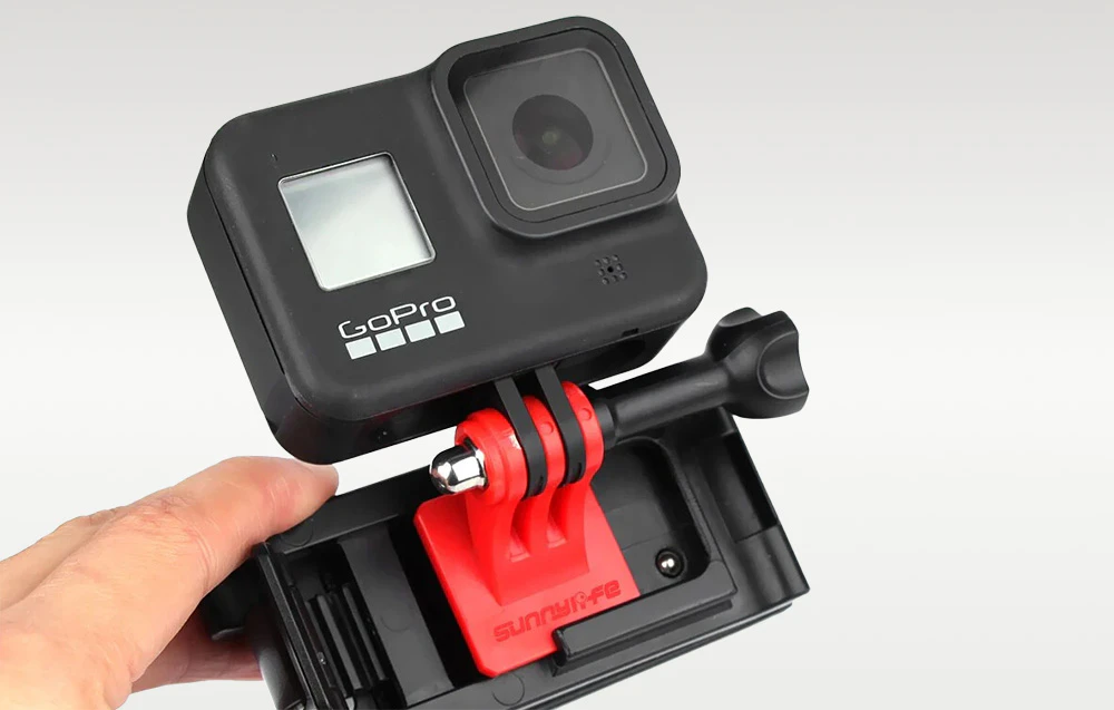 Mână care ține clipul camerei GoPro, arătând cum este montată pe cureaua rucsacului