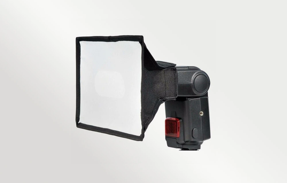 Bliț cu un difuzor softbox pătrat, negru, atașat, pe un fundal deschis și uniform