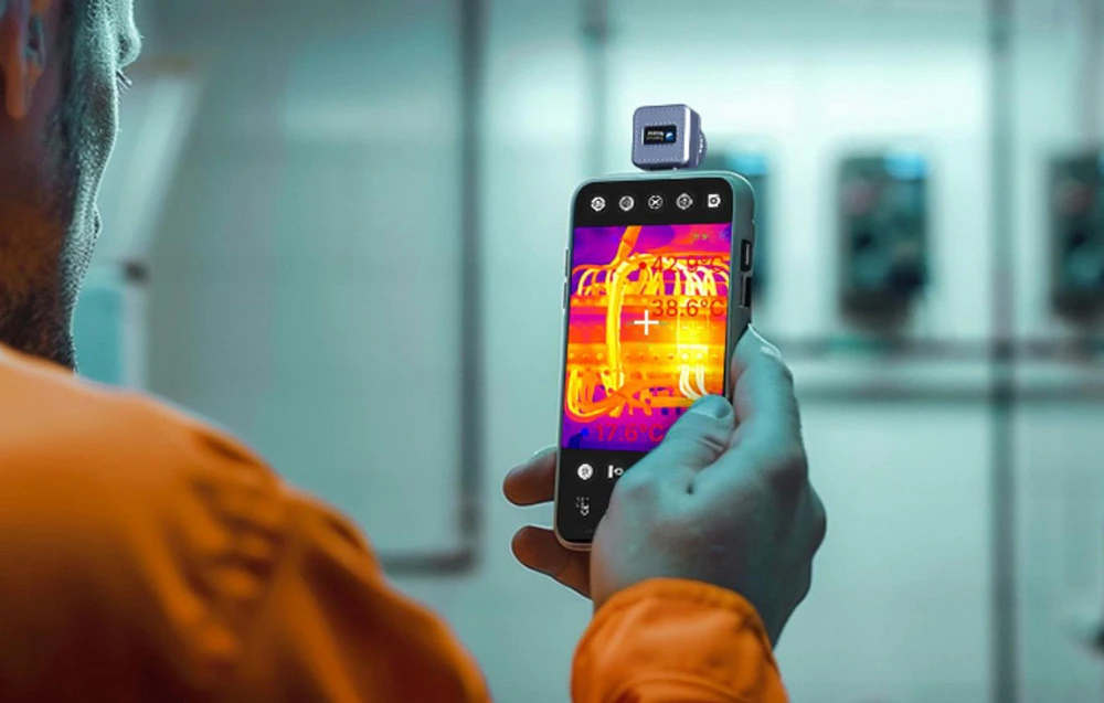 Un angajat se uită la ecranul unui smartphone cu o cameră termică, verificând temperatura cablurilor electrice.