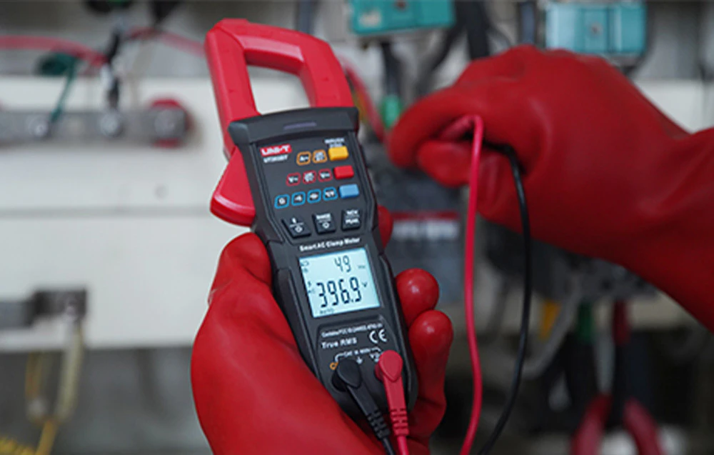 Clește ampermetric UNI-T în mâinile unui electrician care poartă mănuși de protecție în timp ce măsoară tensiunea de curent alternativ.