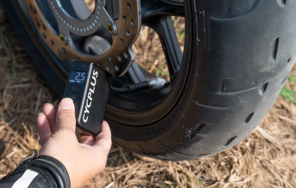 Mână care ține un umflator Cycplus negru la roata unei motociclete cu disc de frână