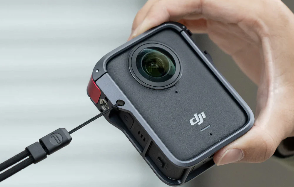 O mână care ține o cameră OSMO 360 într-o carcasă cu o bandă de mână atașată la ea