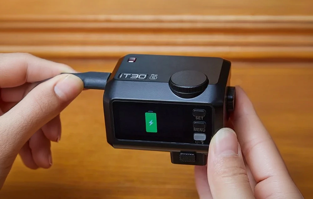 Un mini-blitz Godox iT30Pro S negru conectat manual la un cablu USB-C în timpul încărcării