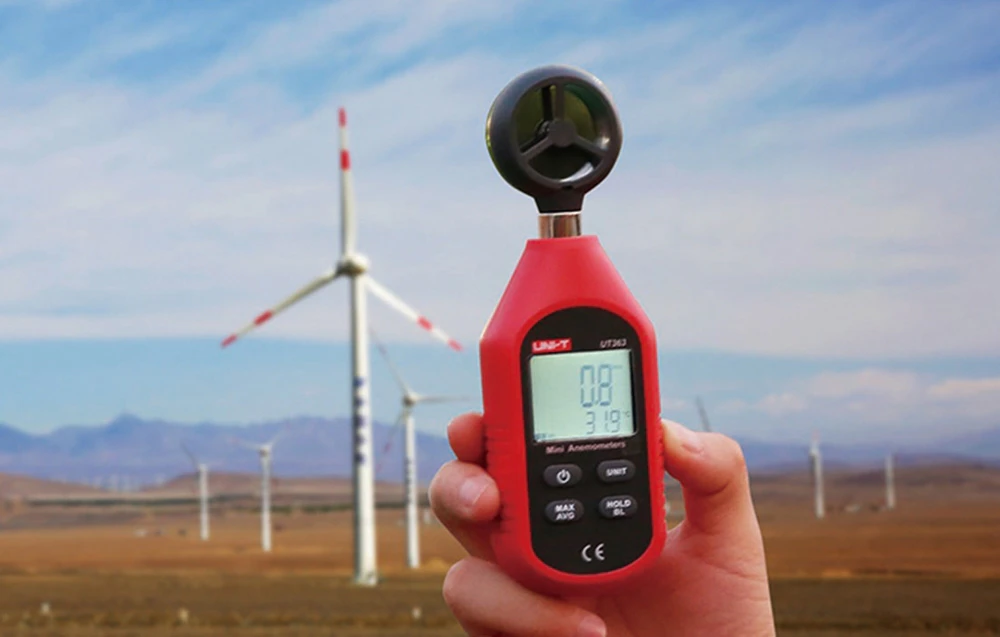 Mini-anemometrul portabil Uni-T măsoară vântul pe fundalul unor mori de vânt