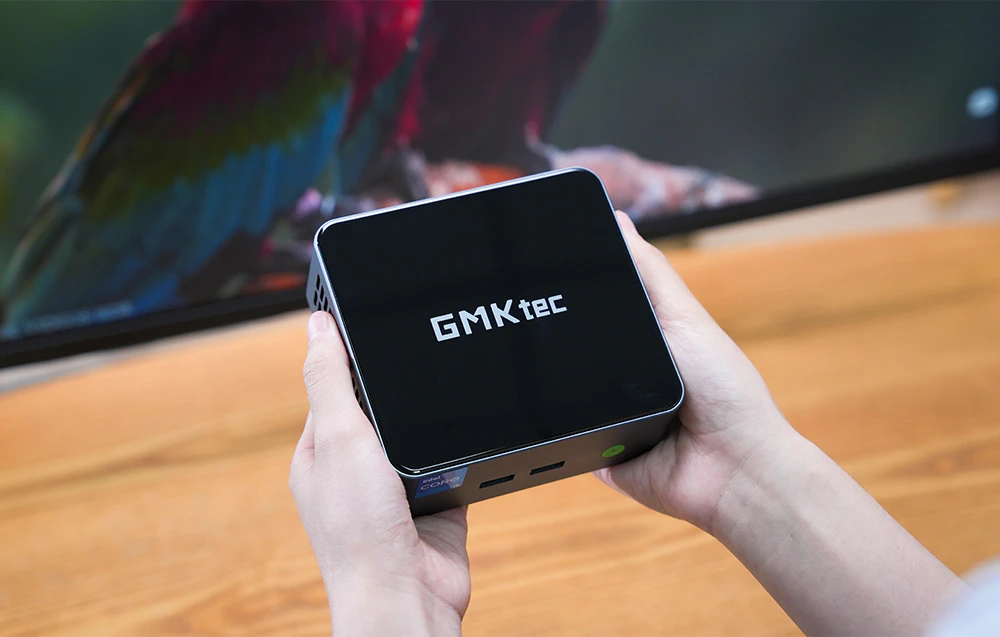 Mini PC-ul GMKtec M3 Pro ținut în mână pe fundalul unui monitor