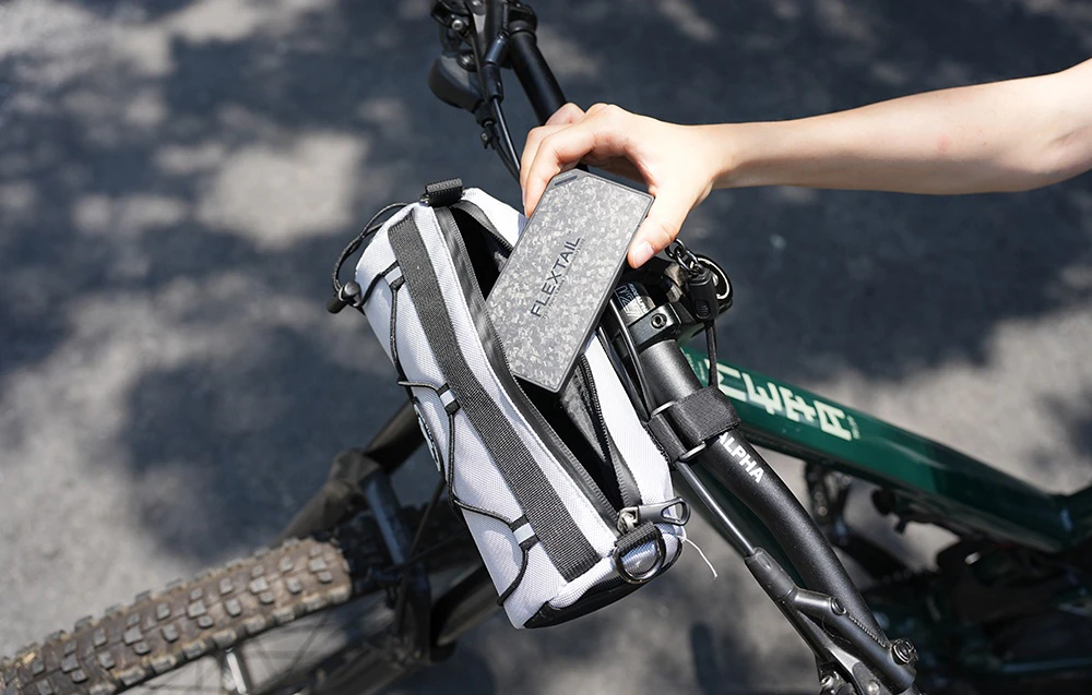 O mână pune bateria externă FLEXTAIL într-o geantă atașată la cadrul unei biciclete.