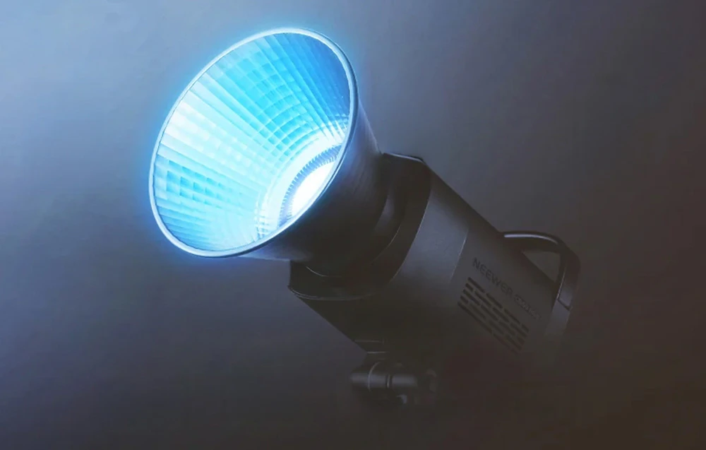 O lampă de studio neagră cu abajur argintiu care emite o lumină albastră puternică și strălucitoare într-o cameră întunecată.