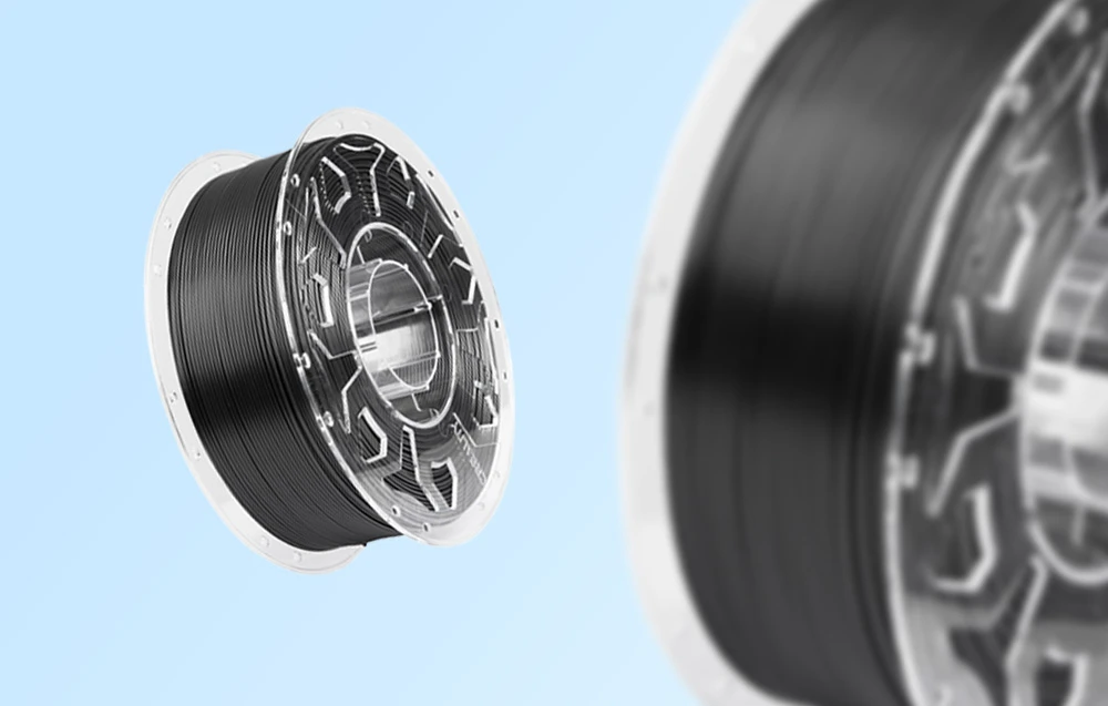 Două bobine cu filament de imprimare 3D negru pe un fundal albastru, una de aproape