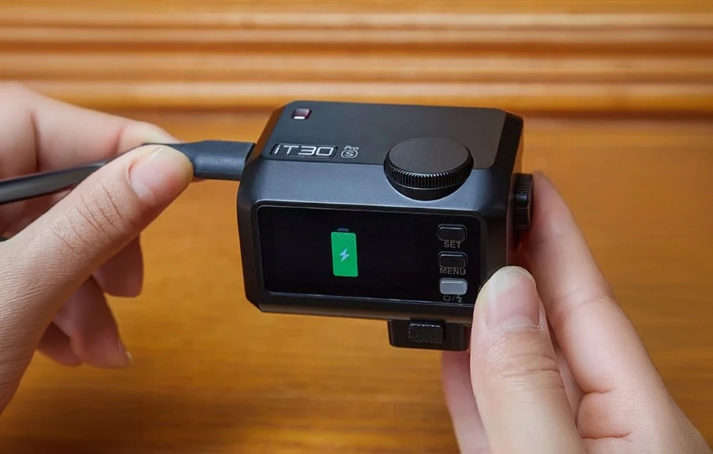 Un mini-blitz Godox iT30Pro S negru conectat manual la un cablu USB-C în timpul încărcării