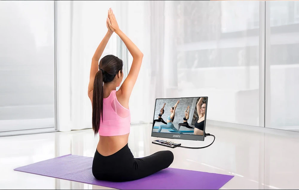 O femeie practică yoga pe un covor violet, uitându-se la un monitor portabil conectat printr-un cablu la un smartphone.