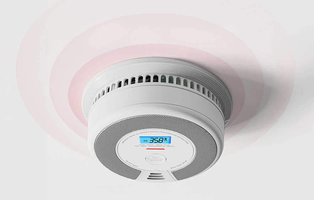 Un senzor de monoxid de carbon montat pe tavan, cu un ecran LCD care afișează 358 PPM și emite unde sonore.