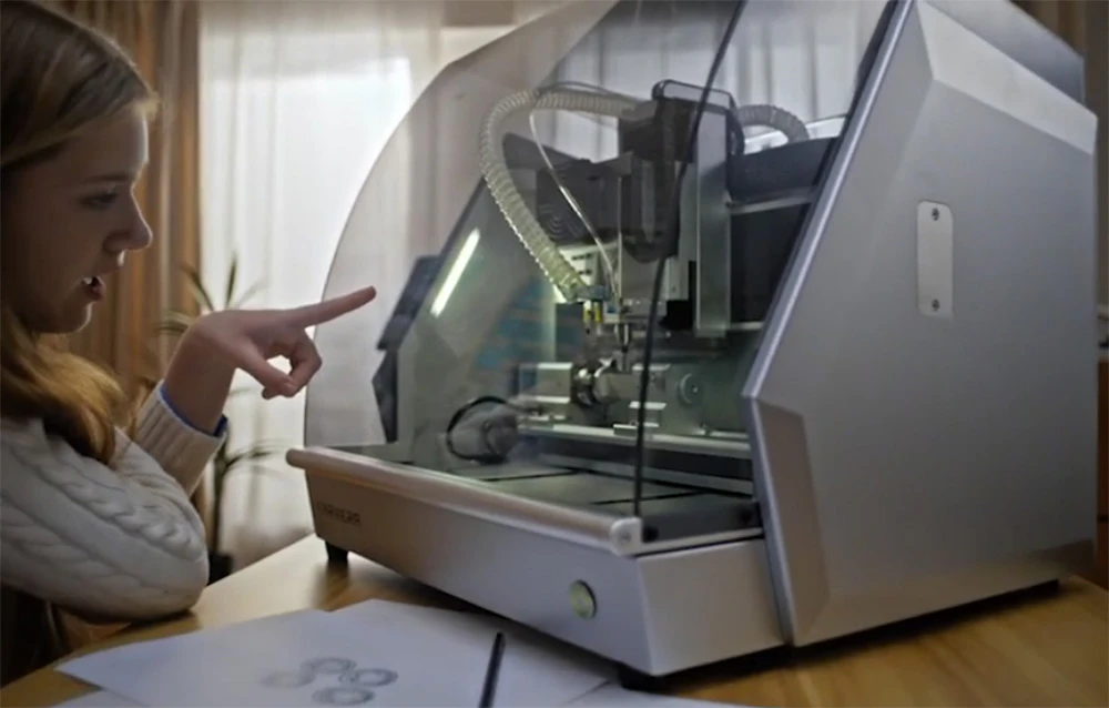 O femeie cu părul blond lângă un router CNC așezat pe un birou