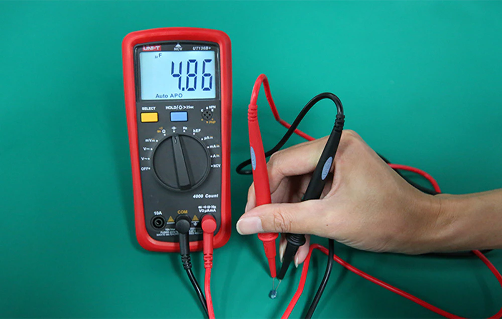 Măsurarea unei componente electronice mici pe un fundal verde folosind sondele multimetrului digital UNI-T.