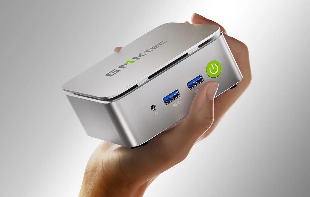 Mini PC argintiu ținut în mână, cu diverse porturi.