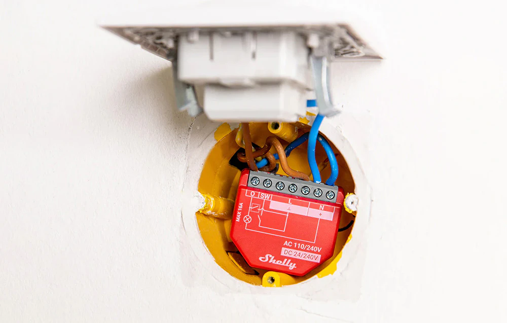Controler roșu montat în interiorul unei cutii încastrate, cu cablajul electric vizibil.