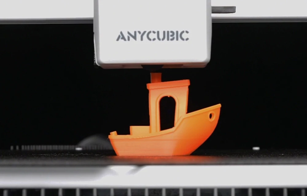 Un model de navă portocaliu fiind imprimat pe platforma imprimantei 3D Anycubic