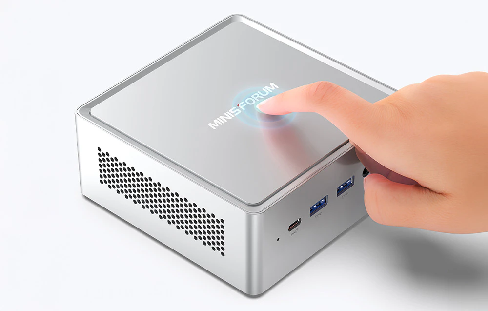 O mână apăsând butonul de alimentare iluminat de pe partea superioară a unui mini PC argintiu de la MINIS FORUM