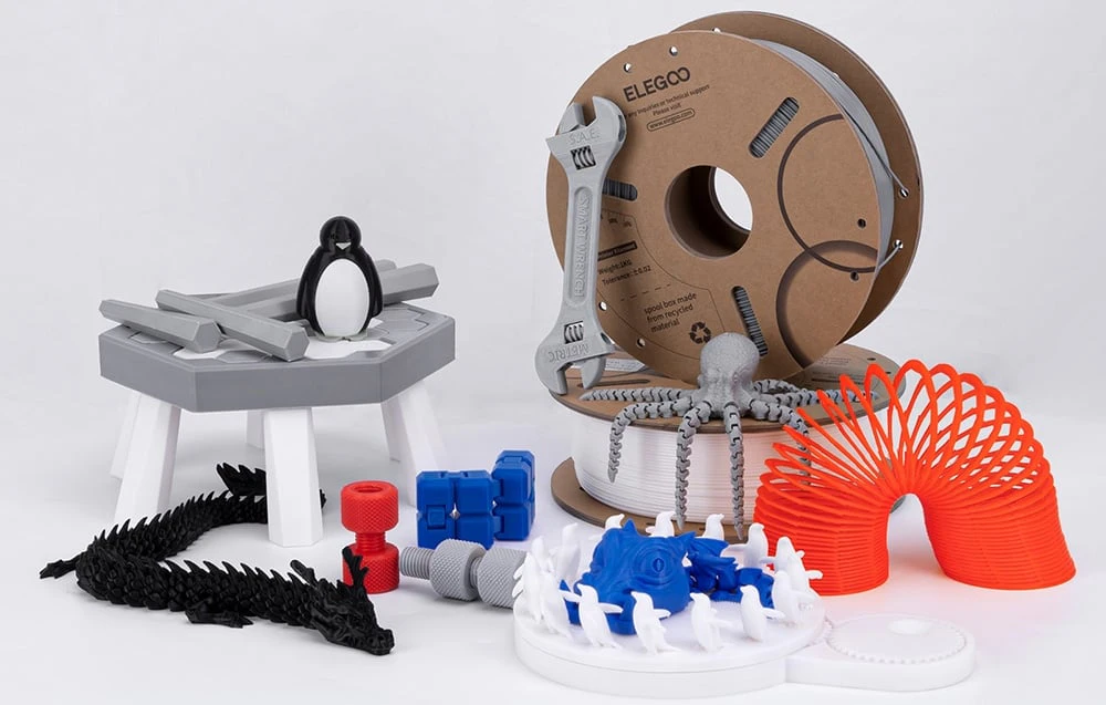 filament alb și gri pentru imprimante 3D înconjurat de diverse modele imprimate 3D