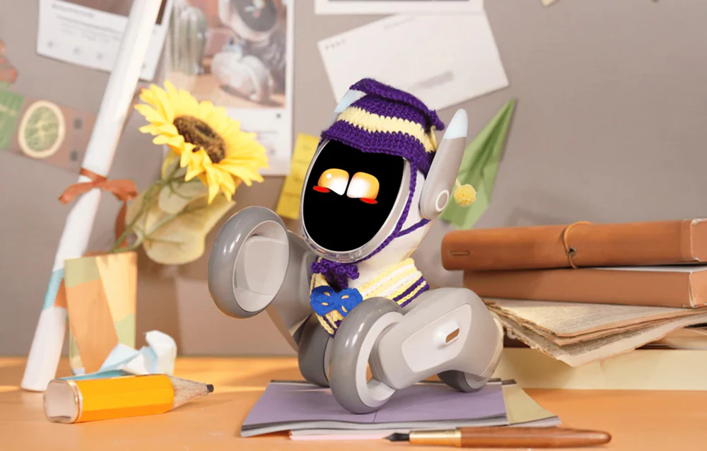 Robotul interactiv Loona în costum de student stă pe un birou plin de bilețele adezive și cărți