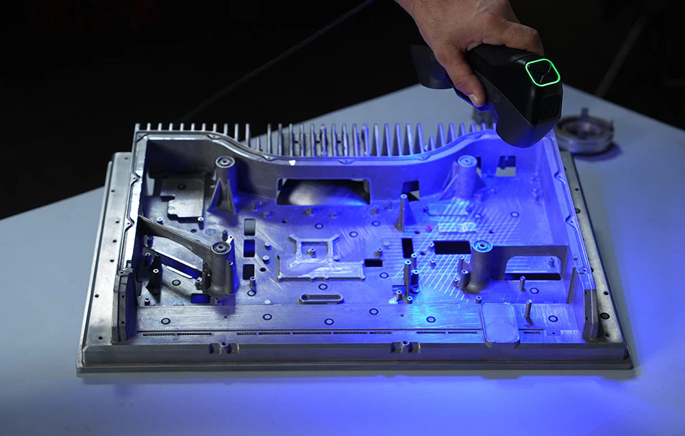 Un bărbat scanează o componentă industrială metalică folosind un scaner 3D cu lumină albastră