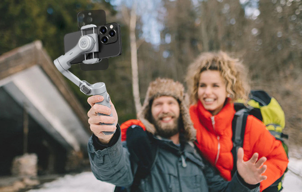 Un cuplu de turiști într-o pădure de iarnă care își fac un selfie cu un gimbal pentru smartphone.