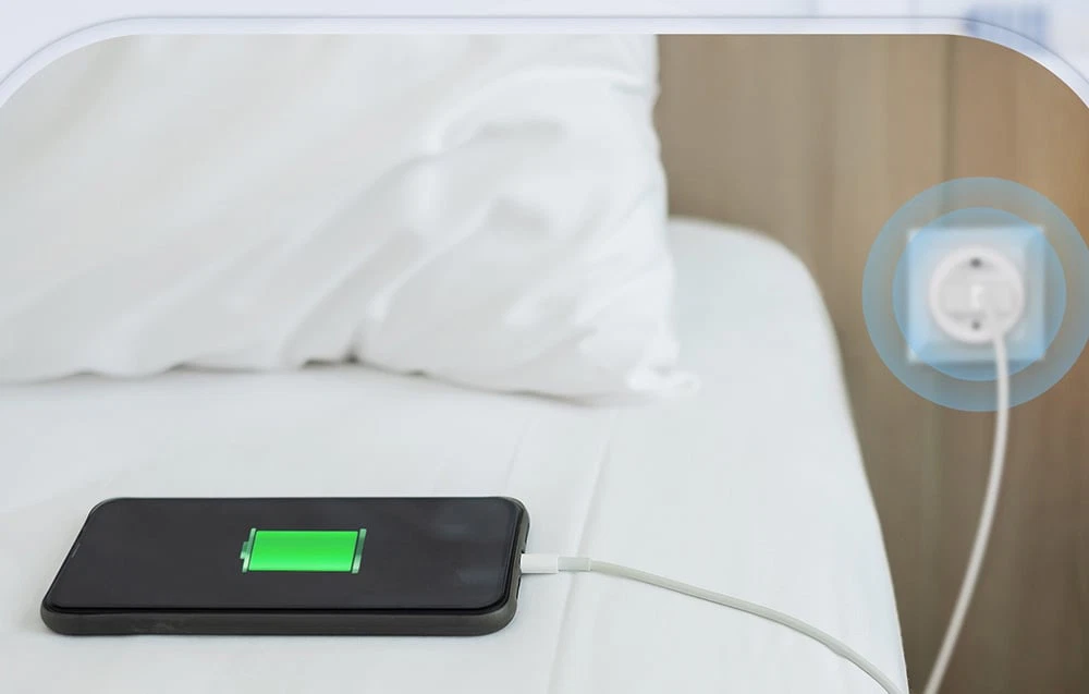 Un telefon care se încarcă pe pat, conectat la o priză cu gestionare la distanță a alimentării.