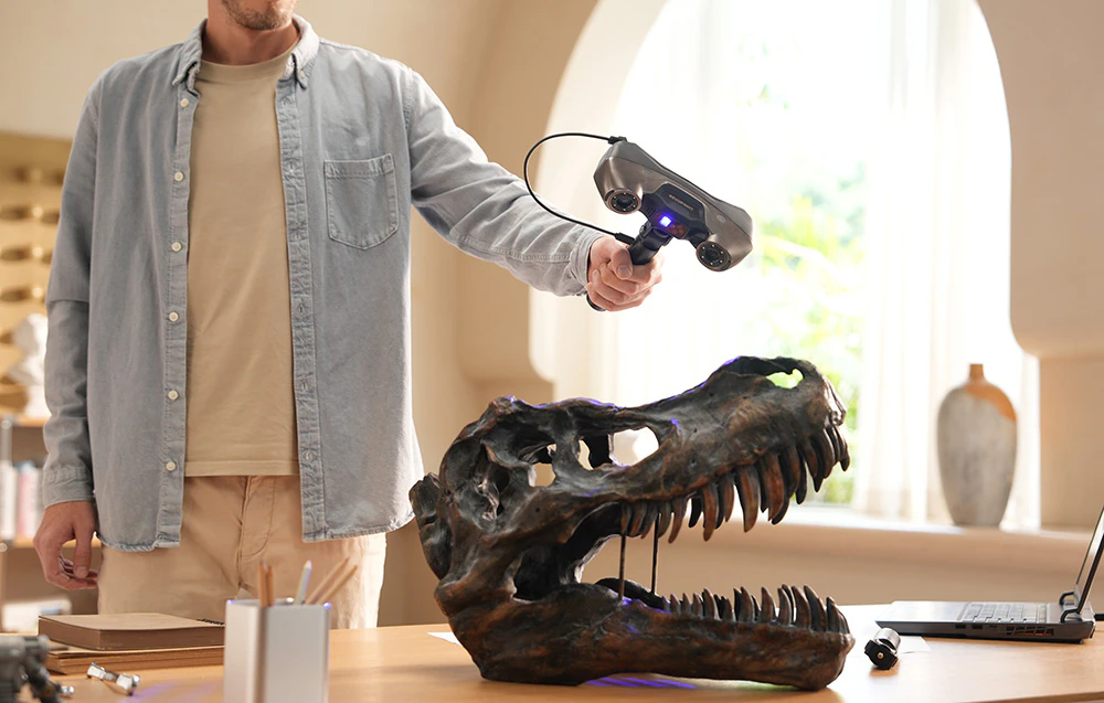 Un bărbat scanează o replică a unui craniu de dinozaur cu un scaner 3D portabil la biroul său
