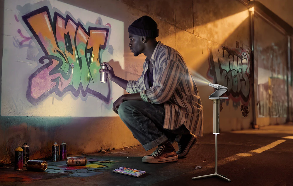 Un bărbat creând graffiti pe un perete pe care proiectorul Zip afișează o imagine