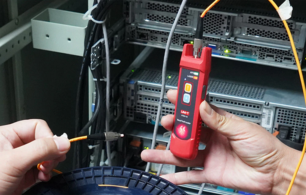 O persoană utilizează un localizator de defecte pentru fibră optică cu laser pentru a verifica continuitatea unui cablu optic într-un dulap de telecomunicații.