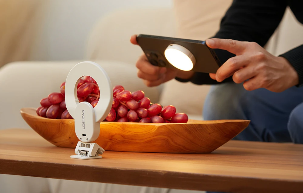 O lumină inelară albă care iluminează un bol cu struguri și un smartphone cu o lumină magnetică circulară