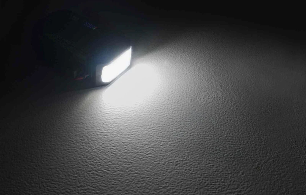 O lumină albă puternică emisă de lampa încorporată a dispozitivului, care luminează o suprafață accidentată în întuneric.