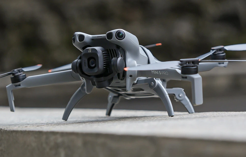 Dronă DJI Mini 5 Pro în picioare pe o suprafață de beton, cu picioare întinse pentru aterizare