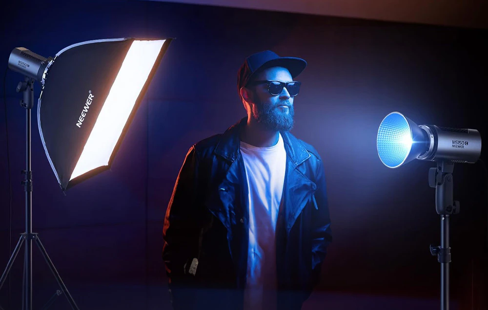 Bărbat cu șapcă și ochelari pozând într-un studio iluminat cu softbox și lampă Neewer