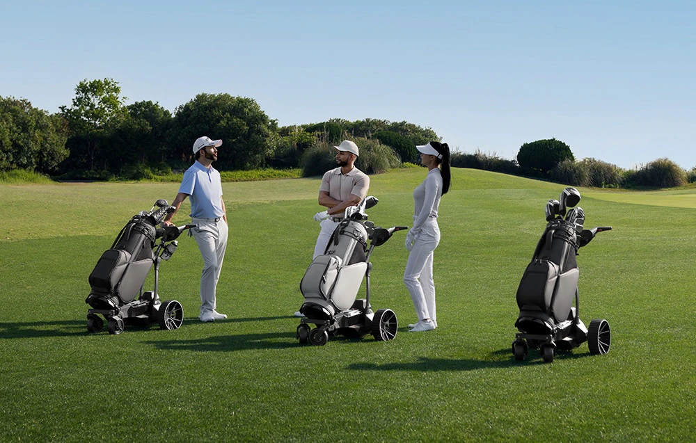 Trei jucători de golf discută pe terenul de golf, înconjurați de trei cărucioare electrice cu saci de golf