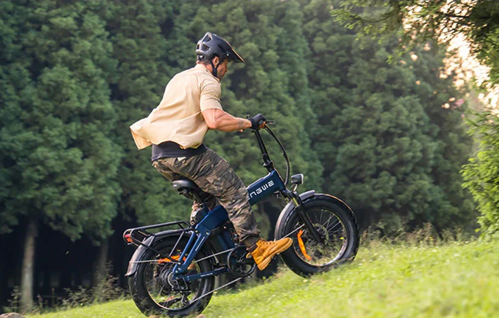 Un bărbat merge cu o bicicletă electrică albastră în sus pe un teren ierbos