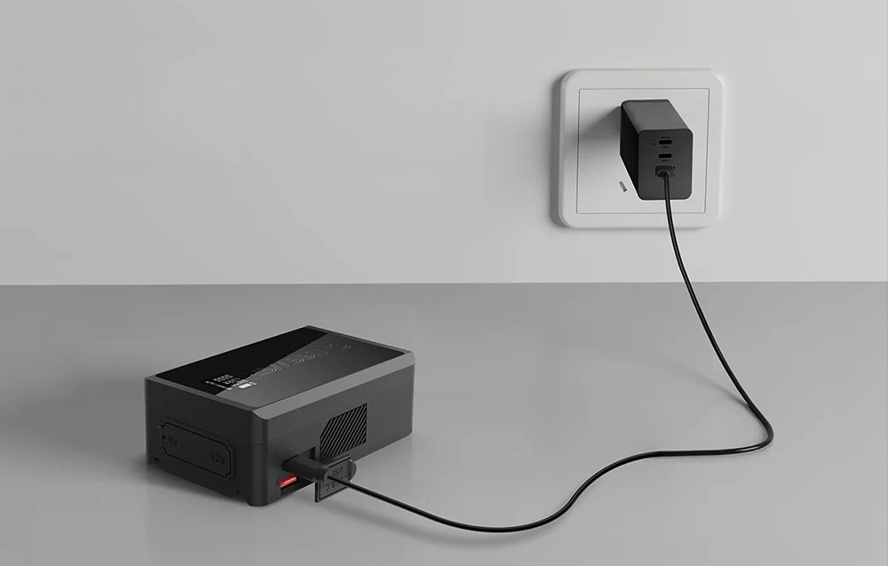 O baterie Neewer conectată printr-un cablu USB la un adaptor de curent alternativ negru, conectat la o priză de perete albă.