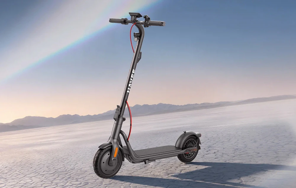 Un scuter electric negru cu inscripția „NAVEE” și un cablu roșu se află pe un sol crăpat, de culoare deschisă, sub un cer cu un curcubeu