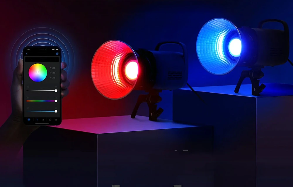 Două lămpi de studio care emit lumină roșie și albastră și o mână care ține un smartphone cu o rotiță de selectare a culorilor.