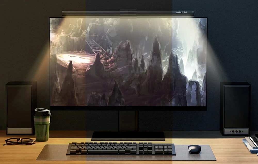 Monitor pe birou cu o lampă atașată, lângă o tastatură, mouse, cană și ochelari