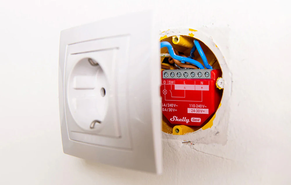 Controlerul plasat în perete în spatele unei prize electrice, arătând metoda de instalare încastrată.