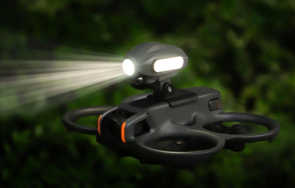 Drone în zbor pe un fundal verde, cu un adaptor universal și o lampă LED aprinsă atașată în partea superioară.